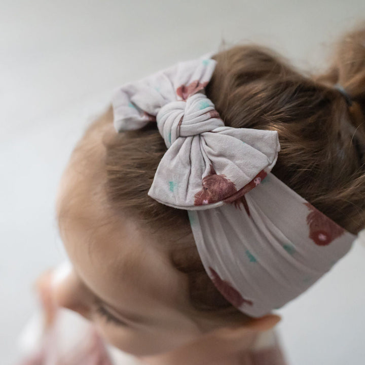 Baby wearing Highland Cow print turban headband with pre-tied top bow